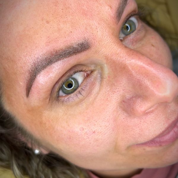 Mujer sonriendo con cejas bien definidas y ojos verdes, retratada en primer plano. Fondo desenfocado que resalta su rostro.