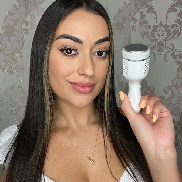 Mujer sosteniendo un dispositivo de belleza facial en un fondo decorativo, mostrando su interés en el cuidado de la piel y las tendencias de belleza.