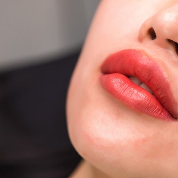 Primer plano de labios maquillados en tonos rojos, mostrando un acabado brillante y bien definido, ideal para resaltar la belleza y el cuidado de la piel.